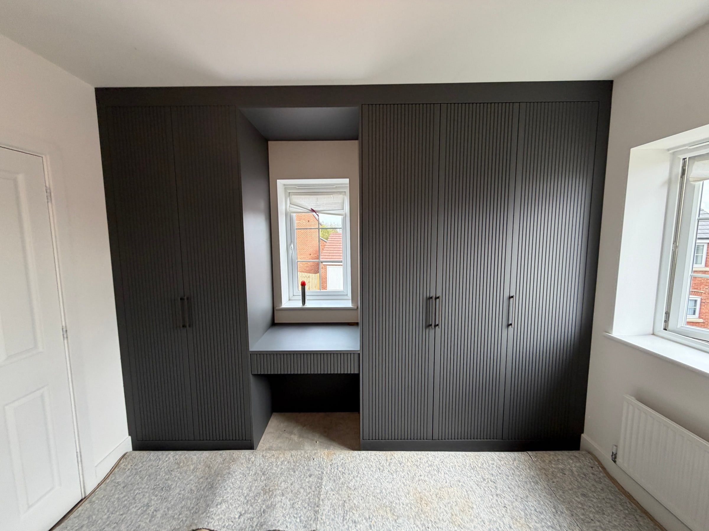 The Barrow upon Soar wardrobes as fitted: dark grey fluted doors either side of the window, joined by a flyover above the dressing space