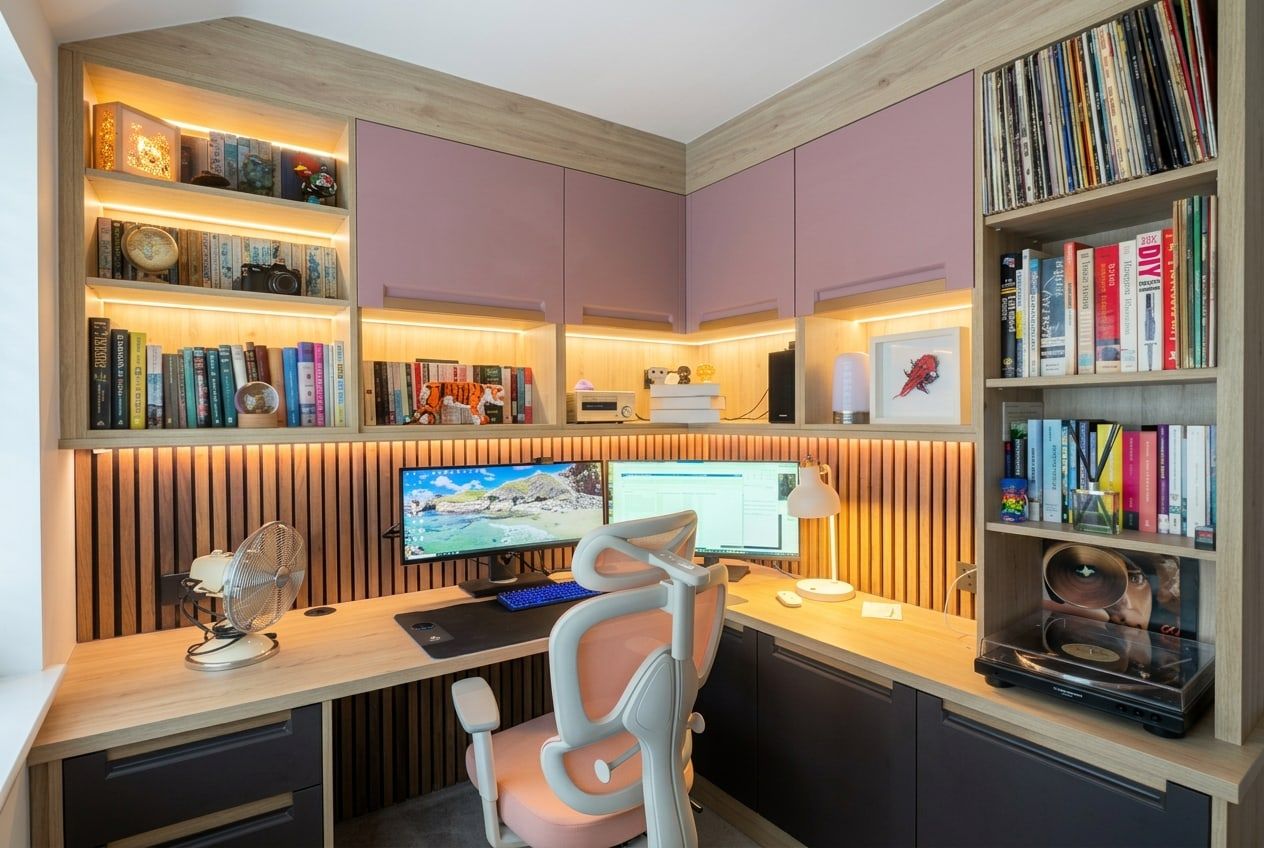 Fitted home office in Bramcote: dusky pink wall cupboards over lit oak-effect shelves, a slatted wall behind the L-shaped desk, coffee supermatt drawers and a tall bookcase