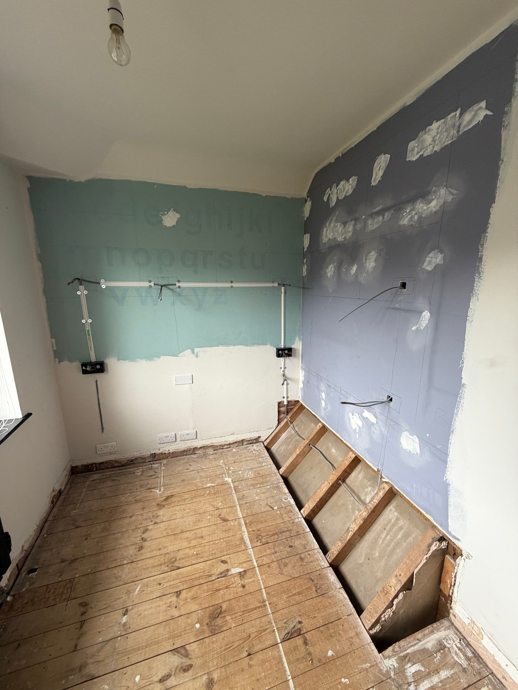 The Bramcote room before: bare floorboards, patched walls and a boxed-in pipe run along the floor