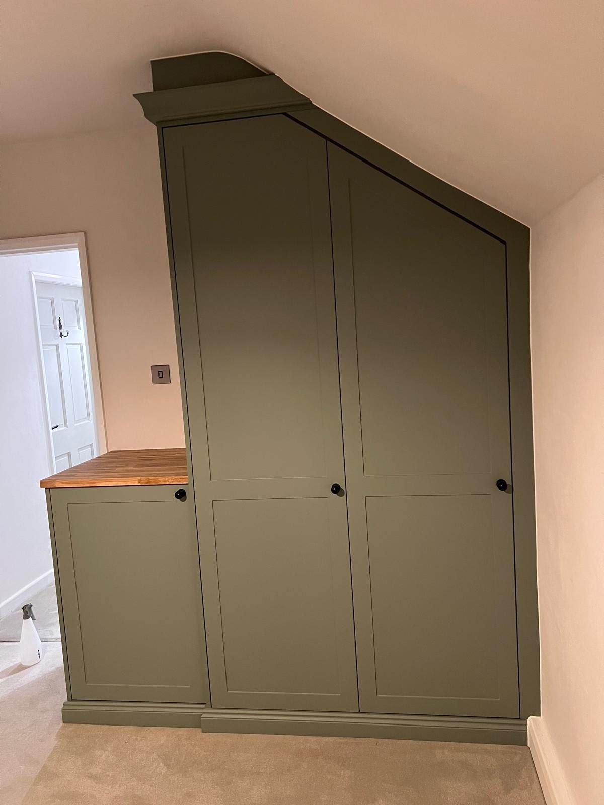 A reed green Contemporary Shaker wardrobe in Loughborough, angled at the top to follow a sloping ceiling, beside a low cupboard with a butcher's block worktop