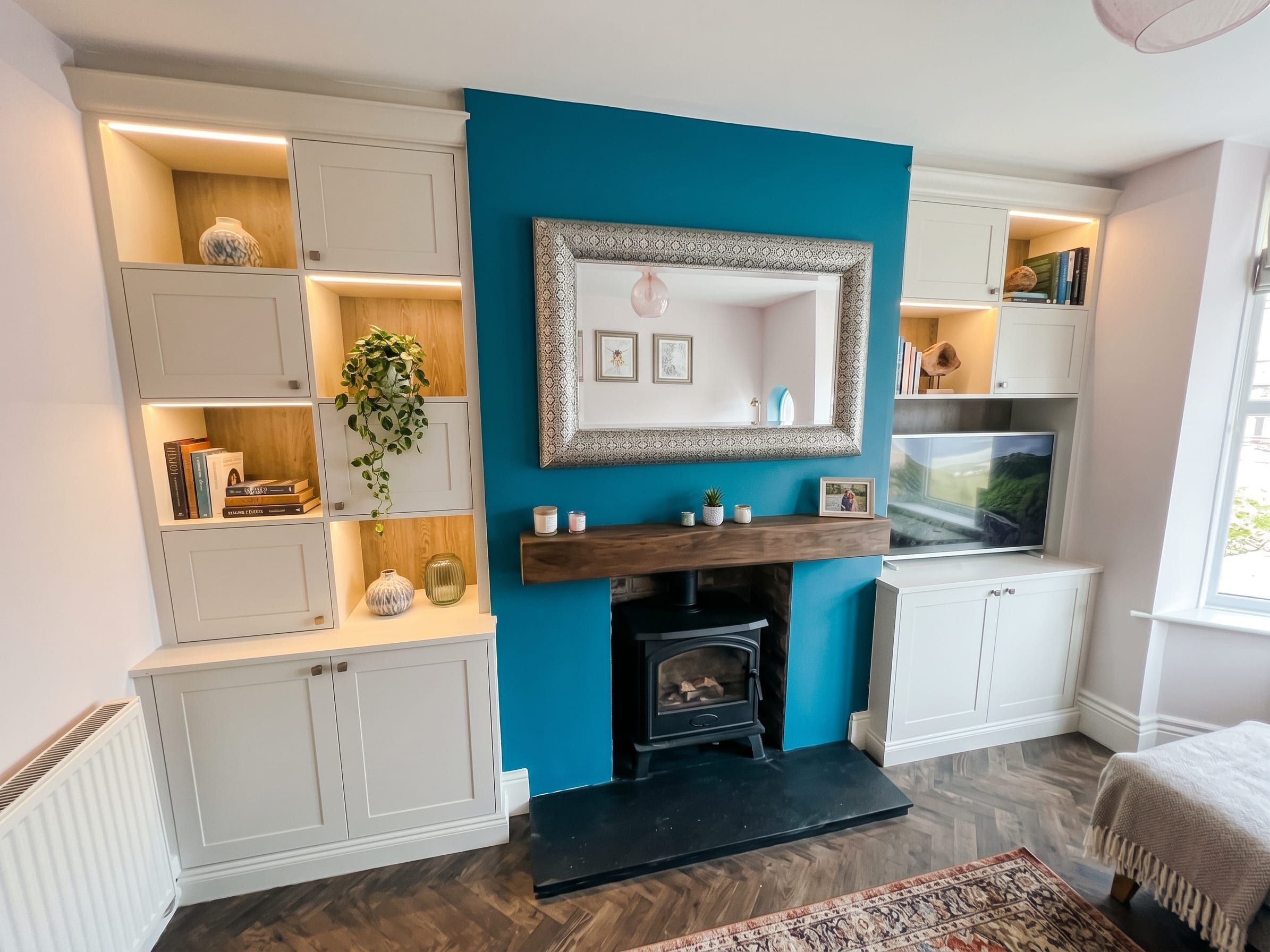 Porcelain white shaker alcove units either side of a chimney breast in Nottingham, with staggered oak-effect open shelves lit by LED strips and the television in the right alcove