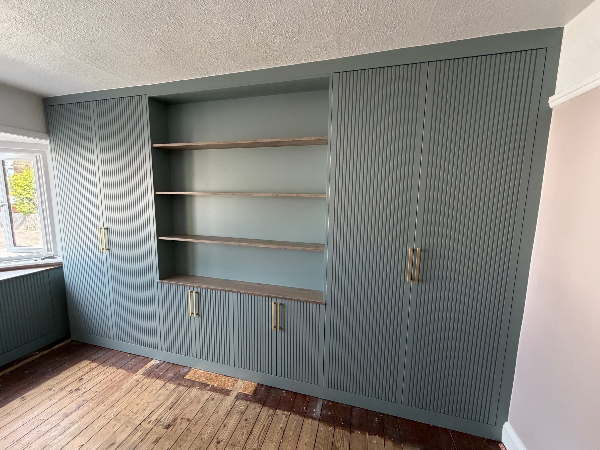 The Sileby wardrobes as fitted: fluted Fjord matt doors either side of open wood-effect shelving, with low cupboards beneath